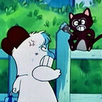 Ein weißer Hund steht wütend vor einem Zaun und fixiert eine schwarze Katze. 