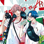 Zwei junge Männer, die auf Reisen sind, stehen sich gegenüber. Einer trägt eine grüne Gürteltasche über der Brust, während der andere eine Kamera in der rechten Hand hält. Sie lächeln sich an und scheinen eine gute Zeit zu haben. 